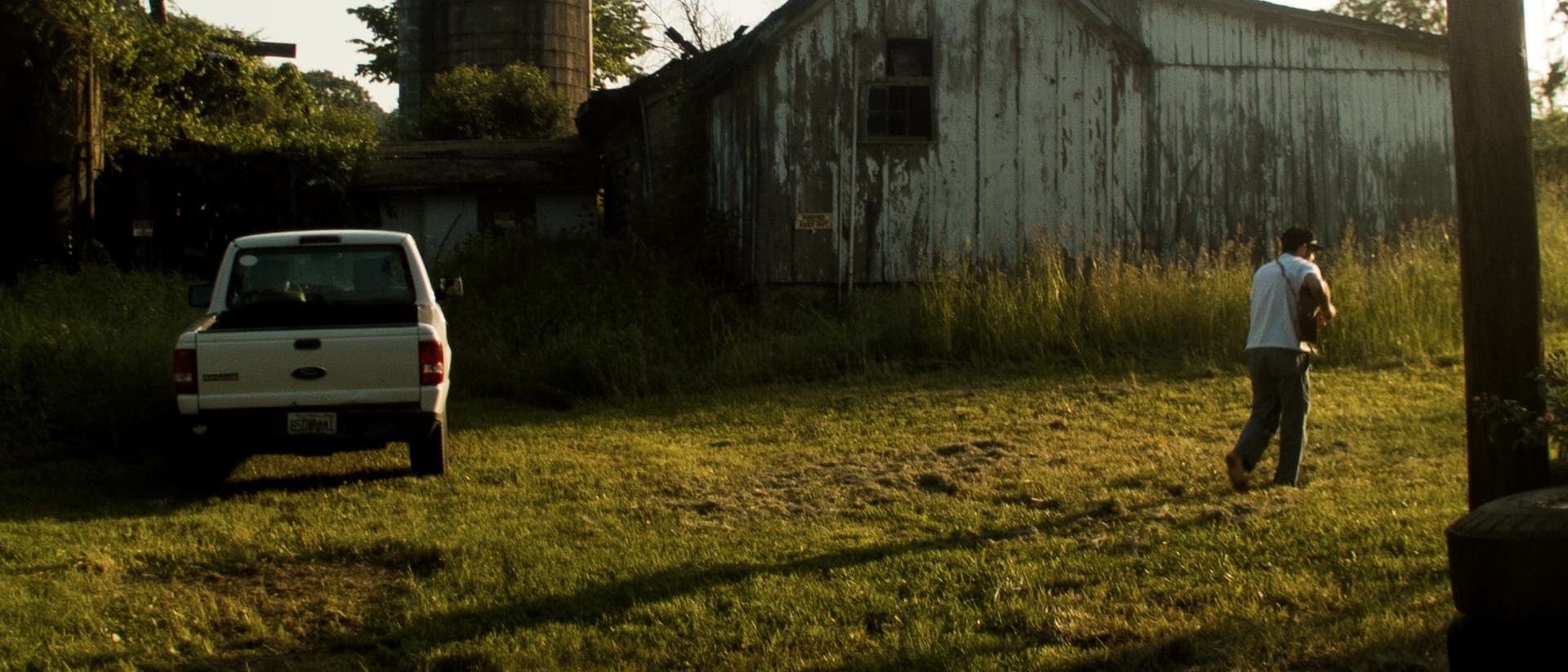 A white barn at golden hour, a pickup parked in the grass, someone walking away.