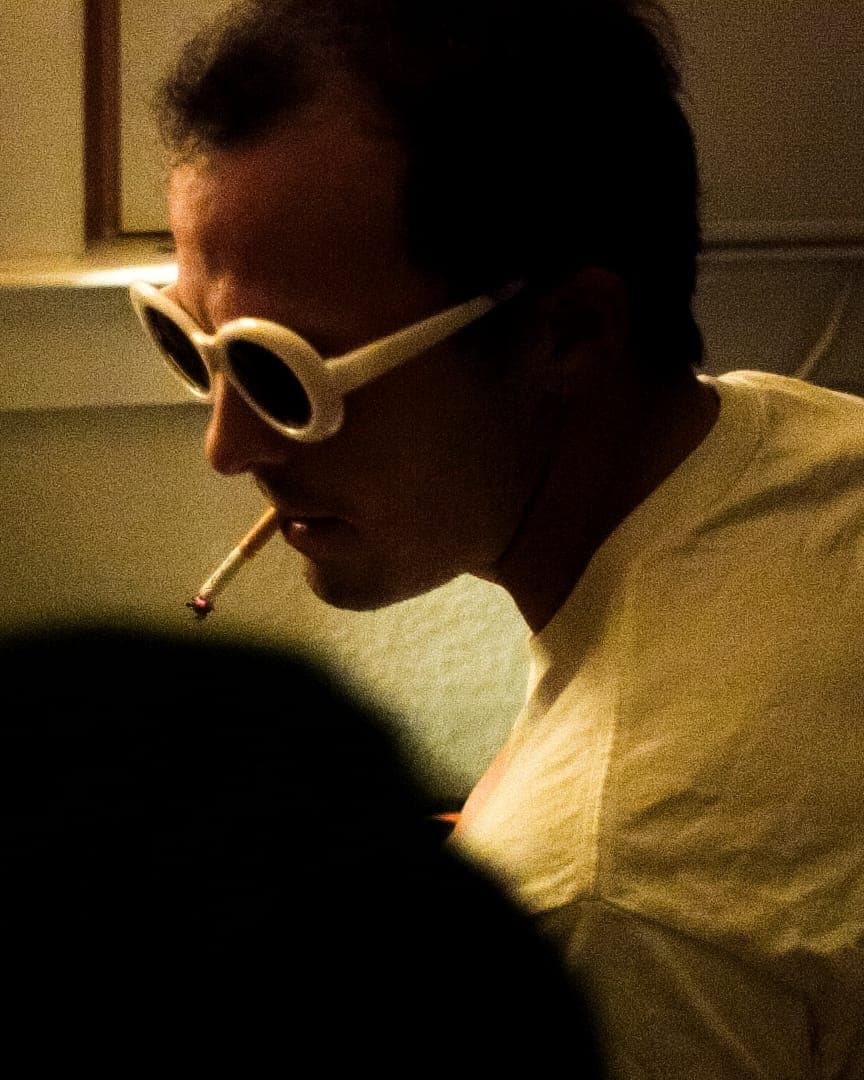 A man in white sunglasses at a piano, in low warm light.