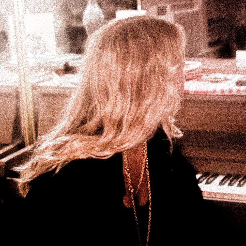 Someone at an upright piano, seen from behind, in warm light.