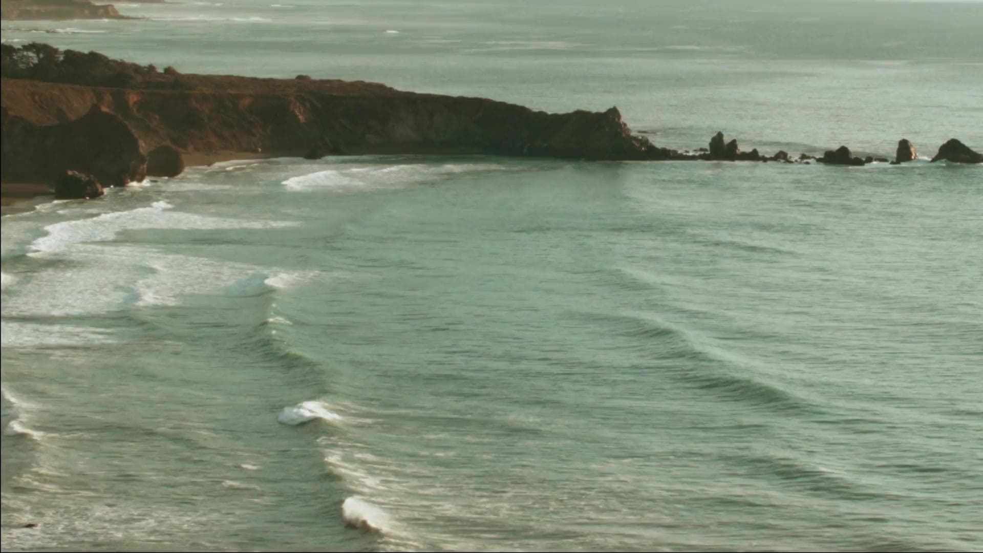 A coastline at dusk. Pale sea, dark rocks, slow waves.